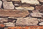 Particolare di un muro in sasso con pietre disposte irregolarmente, ricoperto in parte da licheni rossi e arancioni